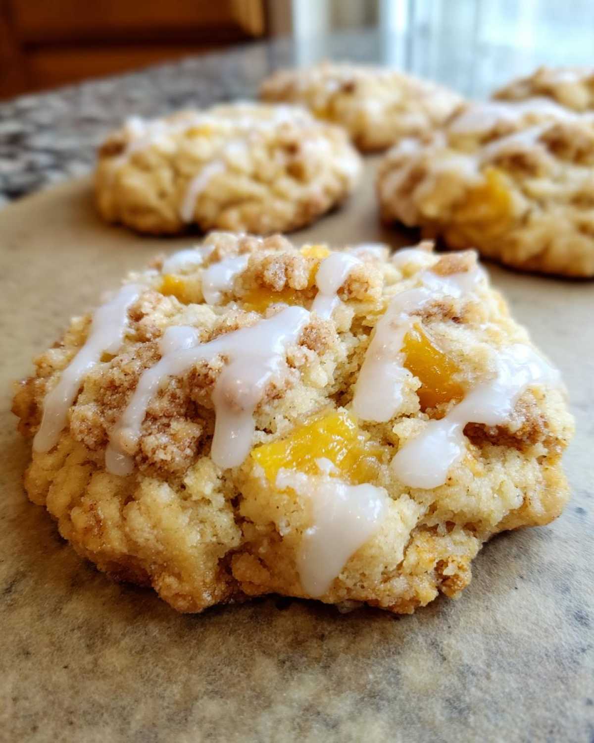 Close-up of a freshly baked peach cobbler cookie with a crumb topping and white icing drizzle.