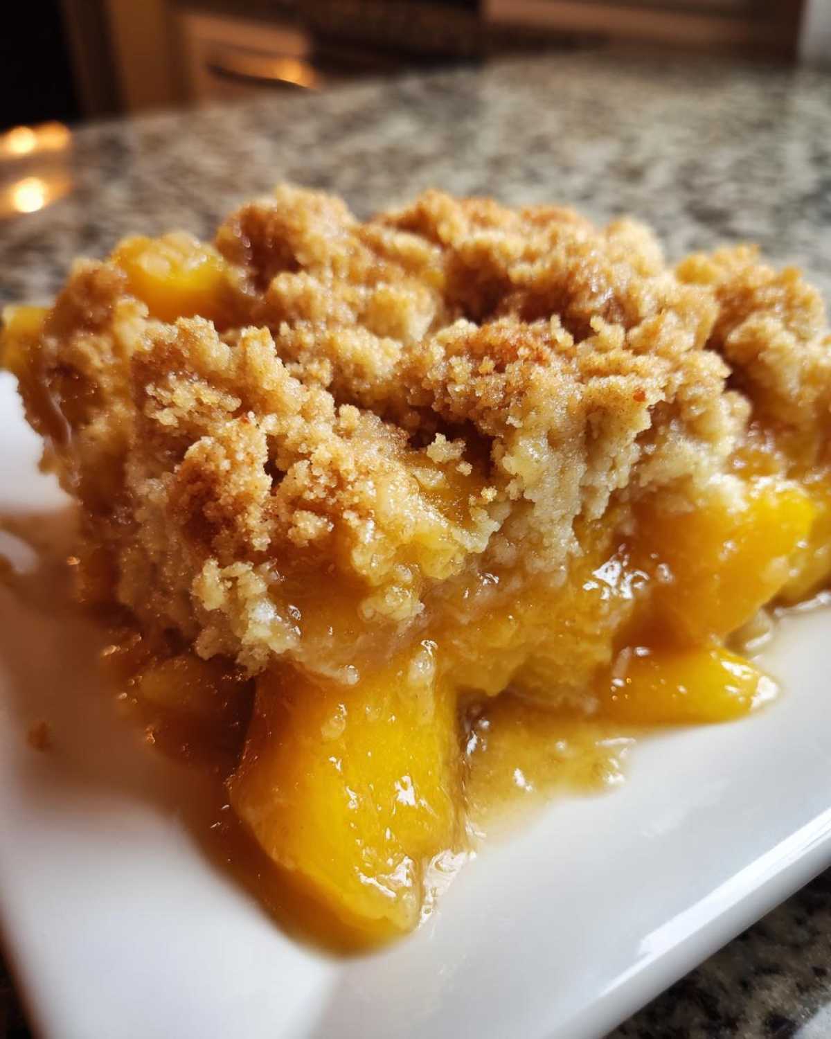 A close-up shot of a single serving of peach cobbler dump cake on a white plate, showing the golden-brown crumble topping and juicy peach filling.