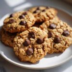 Close-up of several freshly baked peanut butter oatmeal protein cookies with chocolate chips on a white plate.