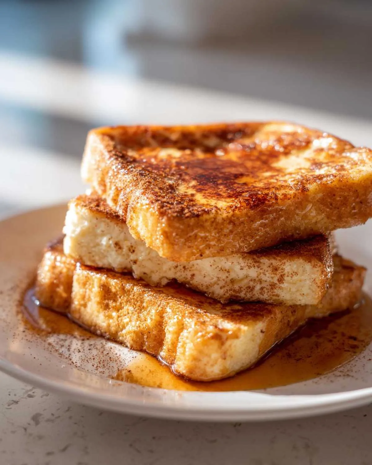 A close-up of a stack of three golden-brown protein french toast slices, drizzled with syrup and sprinkled with cinnamon.