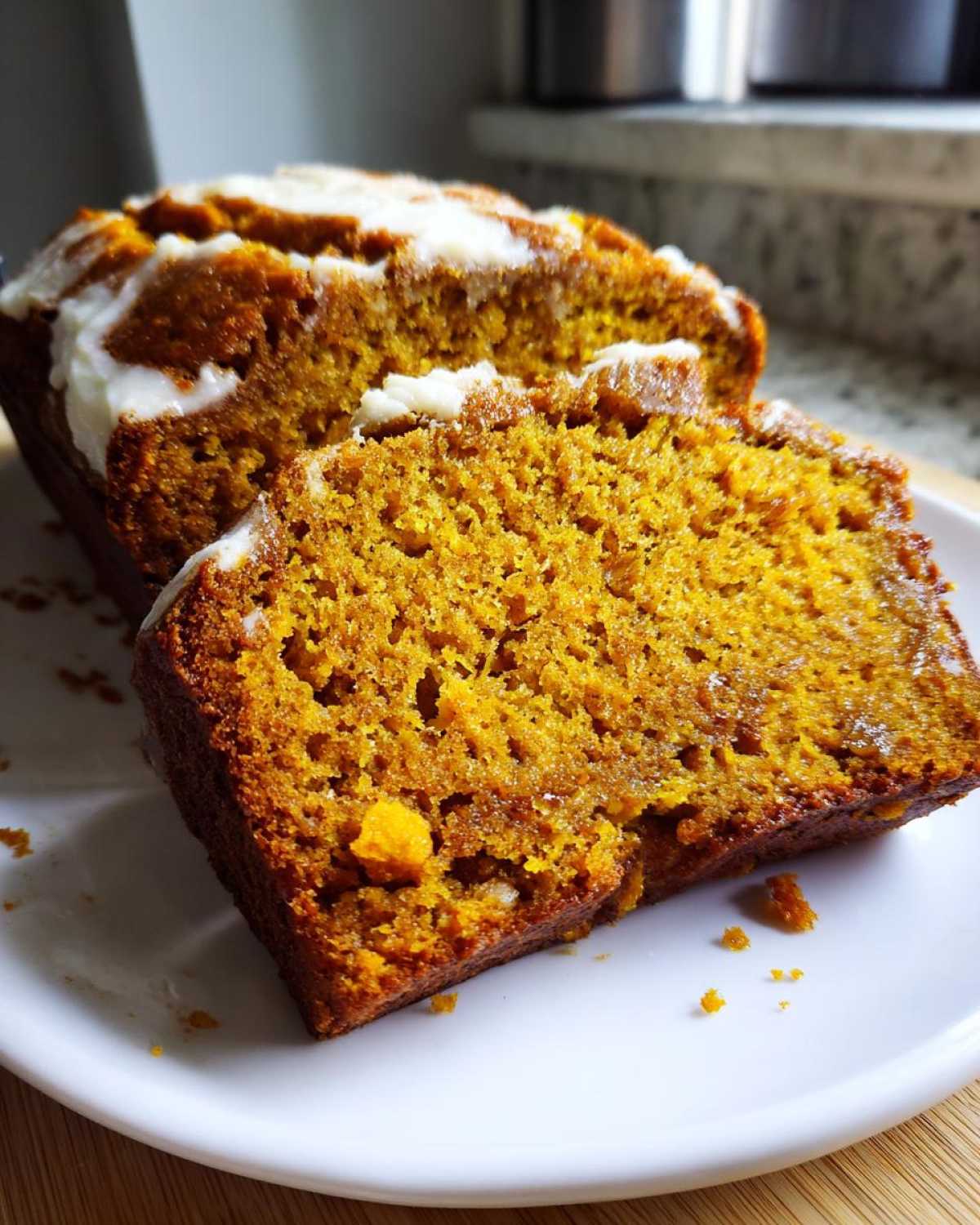 A close-up of a slice of pumpkin bread with cream cheese frosting on a white plate.