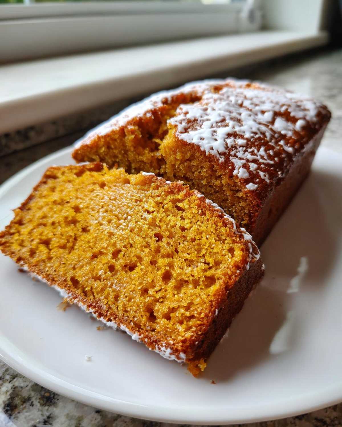 A slice of moist pumpkin bread dusted with powdered sugar, showcasing the bread's texture.