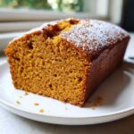 A slice of moist pumpkin bread dusted with powdered sugar, showcasing its texture and color.