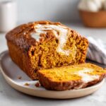 A loaf of pumpkin bread with cream cheese filling, with a slice cut and displayed on a plate.