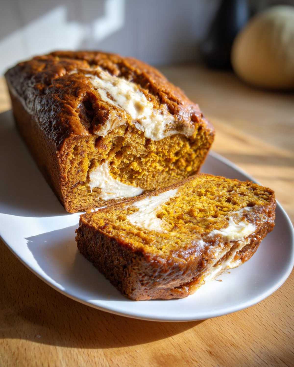 A slice of pumpkin bread with cream cheese filling on a white plate, next to the loaf.