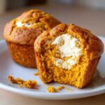 A pumpkin cream cheese muffin with a bite taken out, revealing the cream cheese filling.