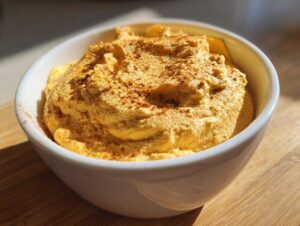 A bowl of pumpkin fluff topped with spice, sitting on a wooden surface.