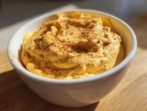 A bowl of pumpkin fluff topped with spice, sitting on a wooden surface.