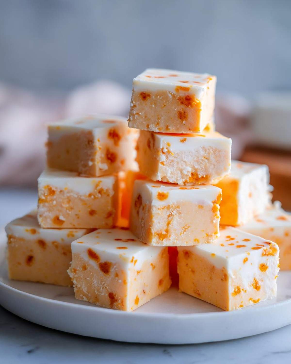 A stack of homemade pumpkin fudge squares on a white plate, showcasing the creamy texture and pumpkin spice swirls.