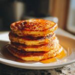 A stack of four pumpkin pancakes is drizzled with syrup on a white plate.