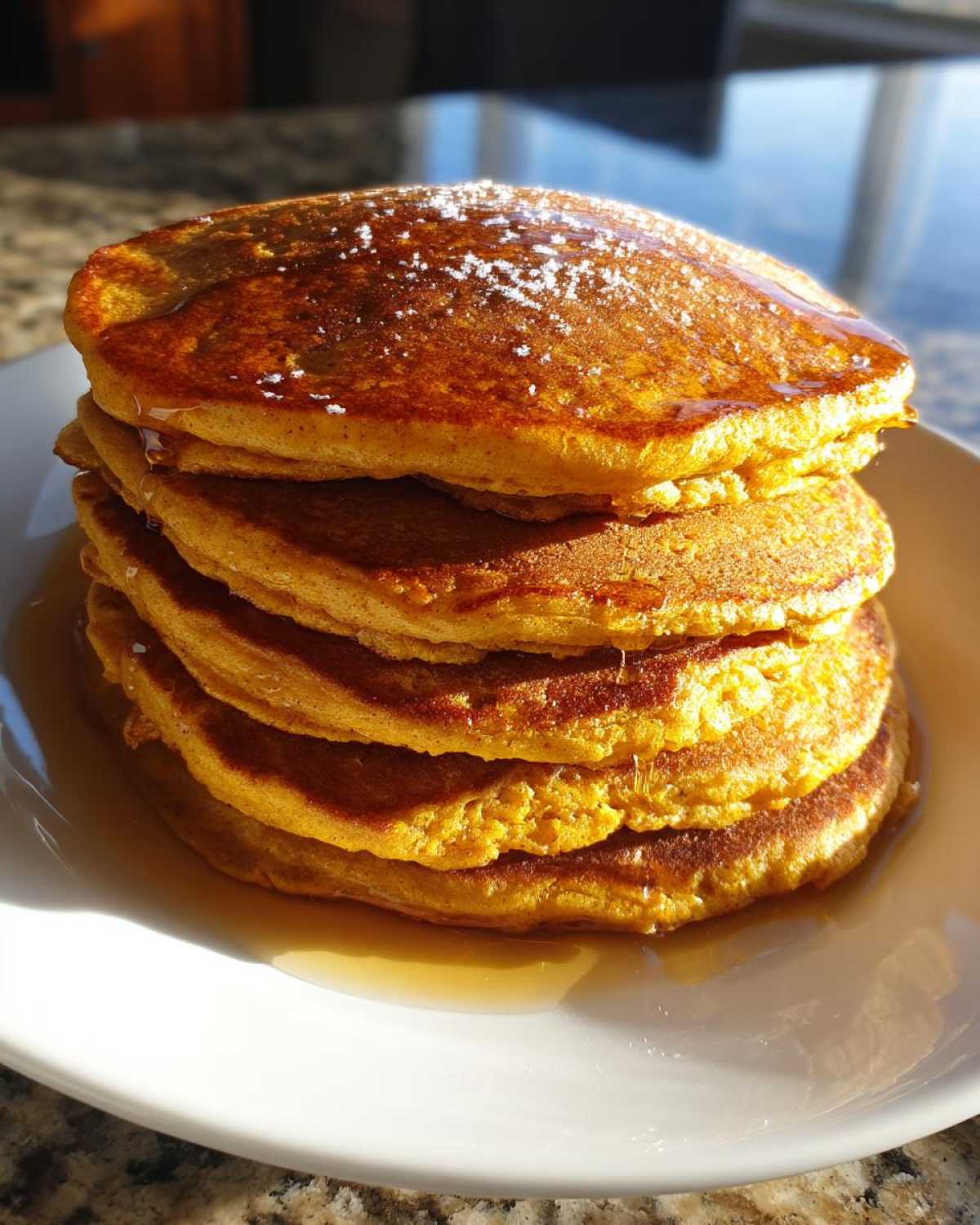 A stack of pumpkin pancakes topped with syrup and powdered sugar on a white plate.
