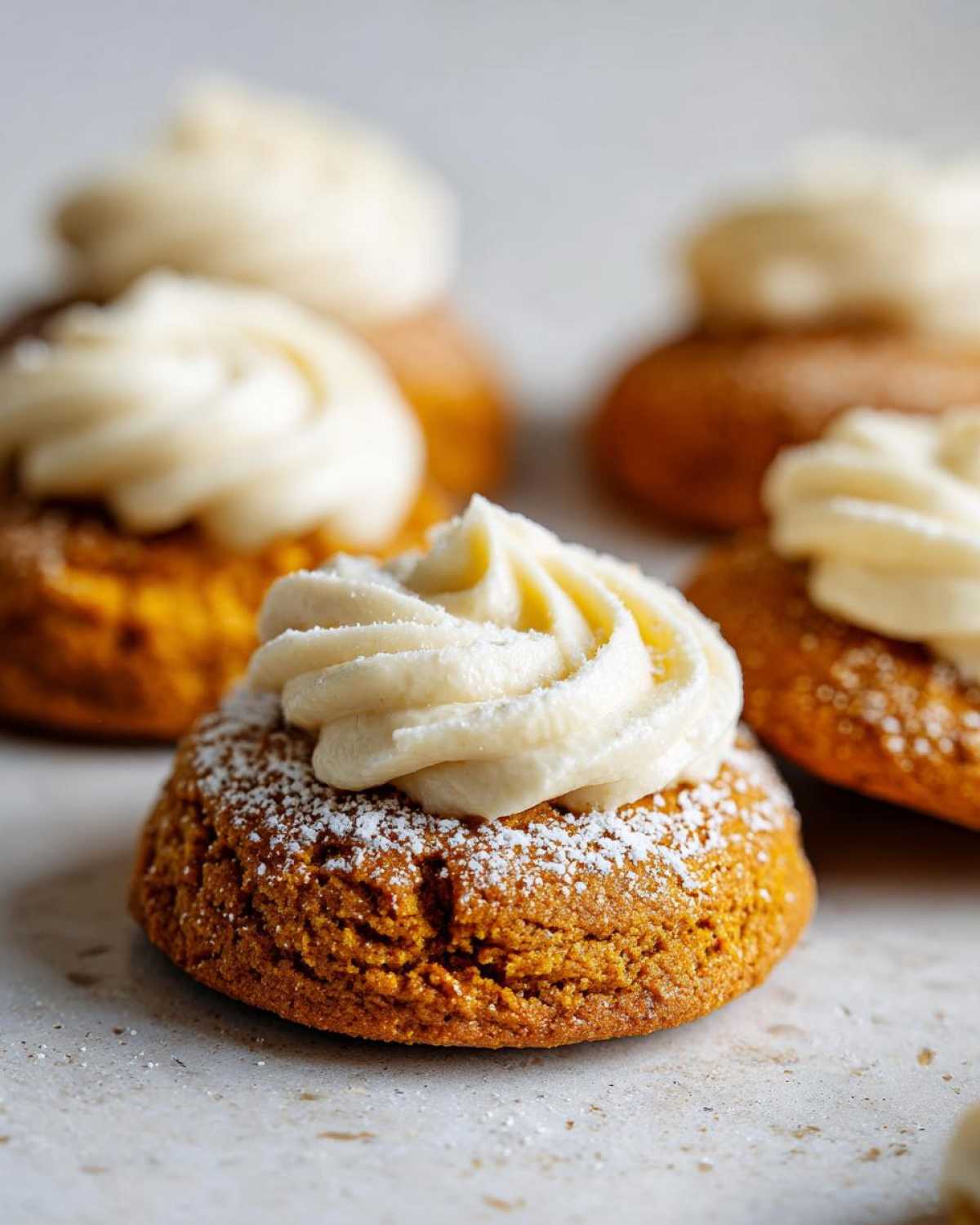 Close-up of pumpkin pie cookies topped with swirl of frosting and powdered sugar.