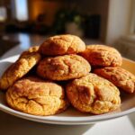 A stack of freshly baked pumpkin snickerdoodle cookies on a white plate, dusted with cinnamon sugar.