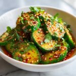 Close-up of a white bowl filled with a vibrant spicy cucumber salad, garnished with sesame seeds and fresh cilantro.