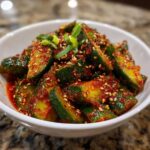 Close-up of a vibrant spicy korean cucumber salad in a white bowl, garnished with green onions and sesame seeds.