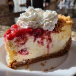 A close-up of a slice of strawberry shortcake cheesecake on a white plate, topped with whipped cream and strawberry compote.