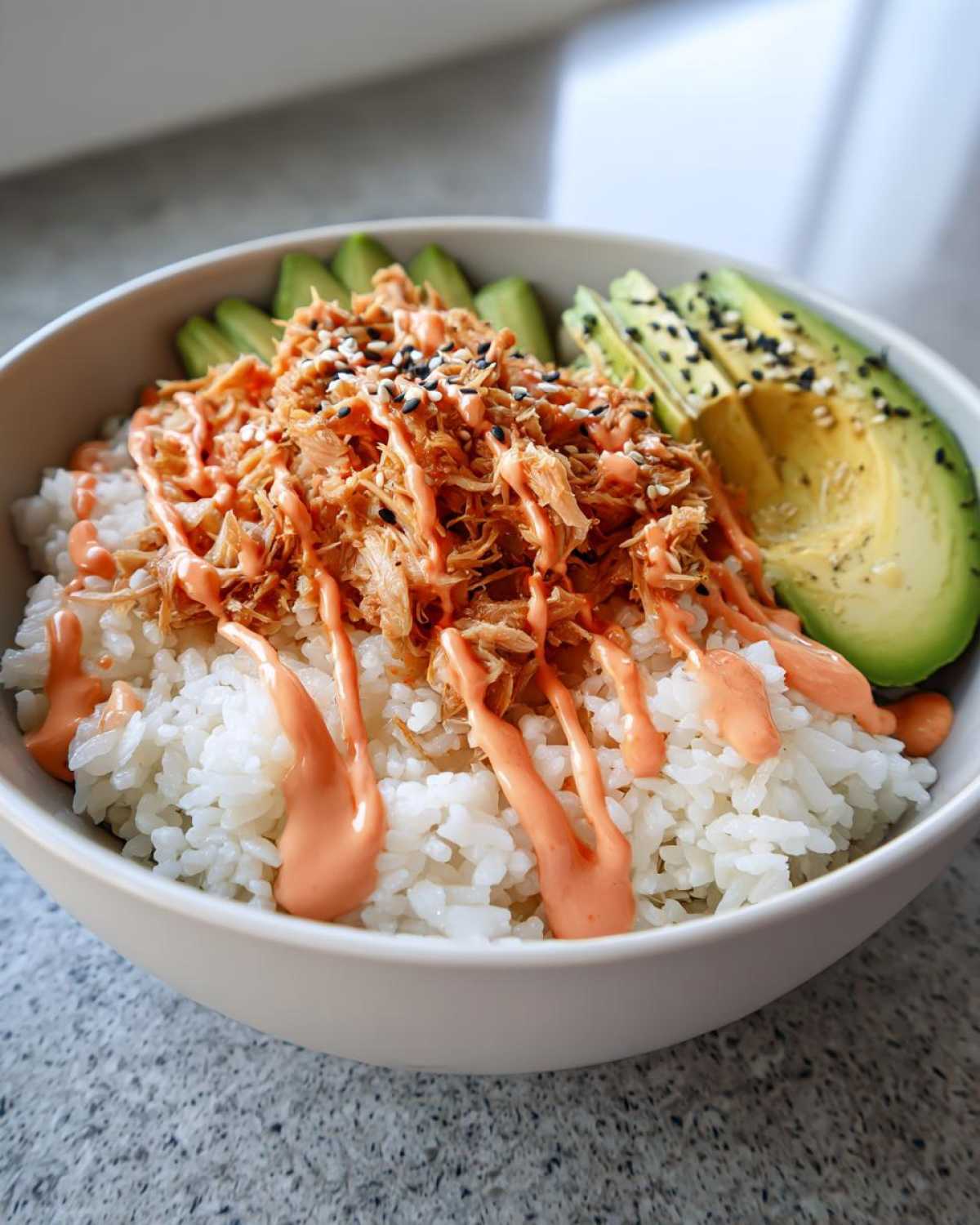 A vibrant tuna and rice bowl topped with spicy mayo, sesame seeds, and sliced avocado.