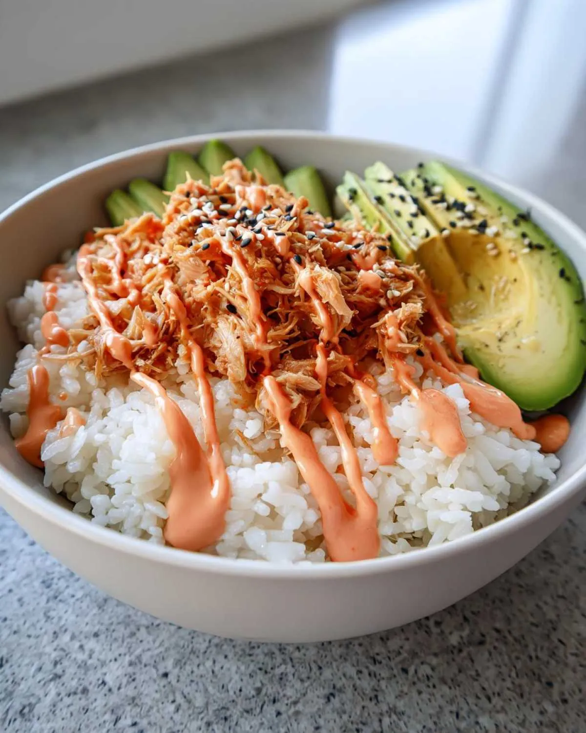 A vibrant tuna and rice bowl topped with spicy mayo, sesame seeds, and sliced avocado.