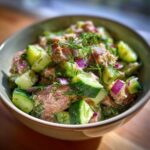 Close-up of a bowl filled with fresh tuna cucumber salad, featuring chunks of tuna, diced cucumbers, red onion, and dill.
