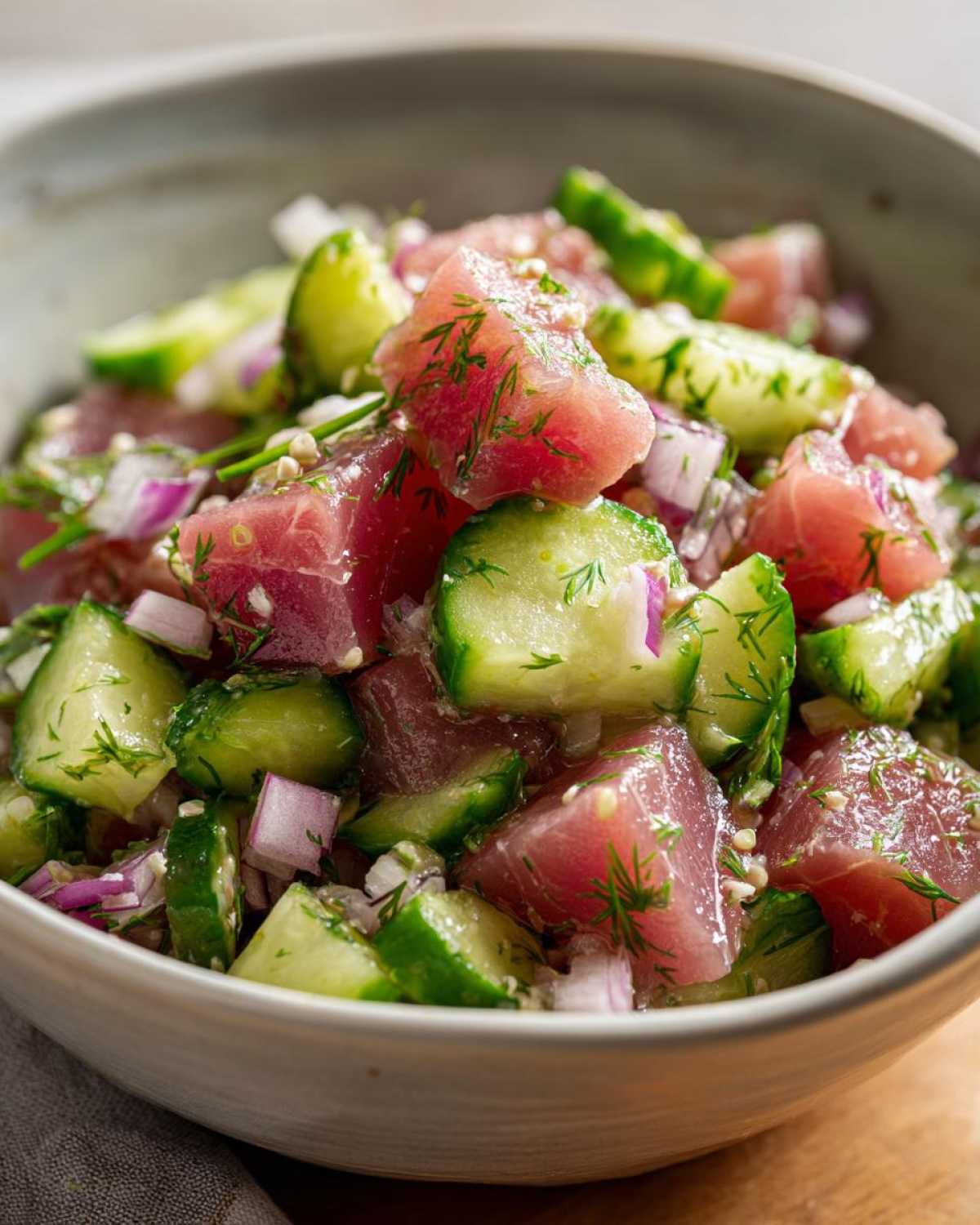 Close-up of a bowl filled with vibrant tuna cucumber salad, featuring diced tuna, cucumber, red onion, and fresh dill.