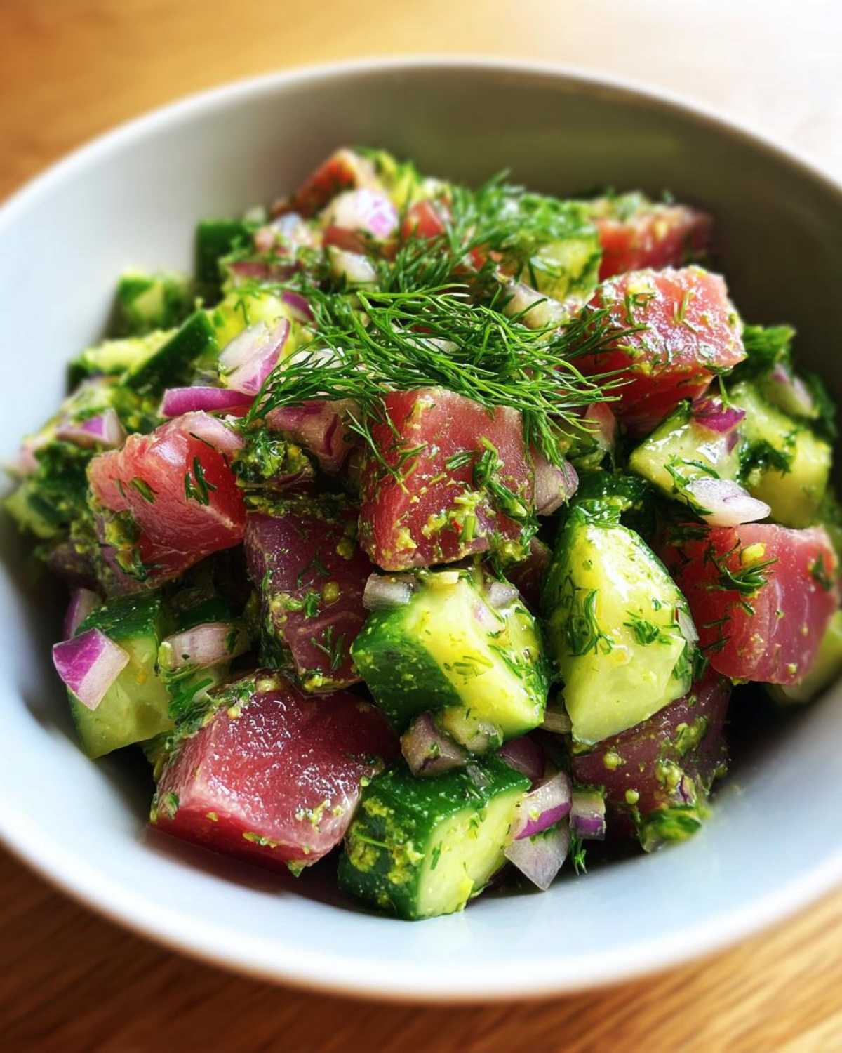 Close-up of a vibrant tuna cucumber salad in a white bowl, garnished with fresh dill.