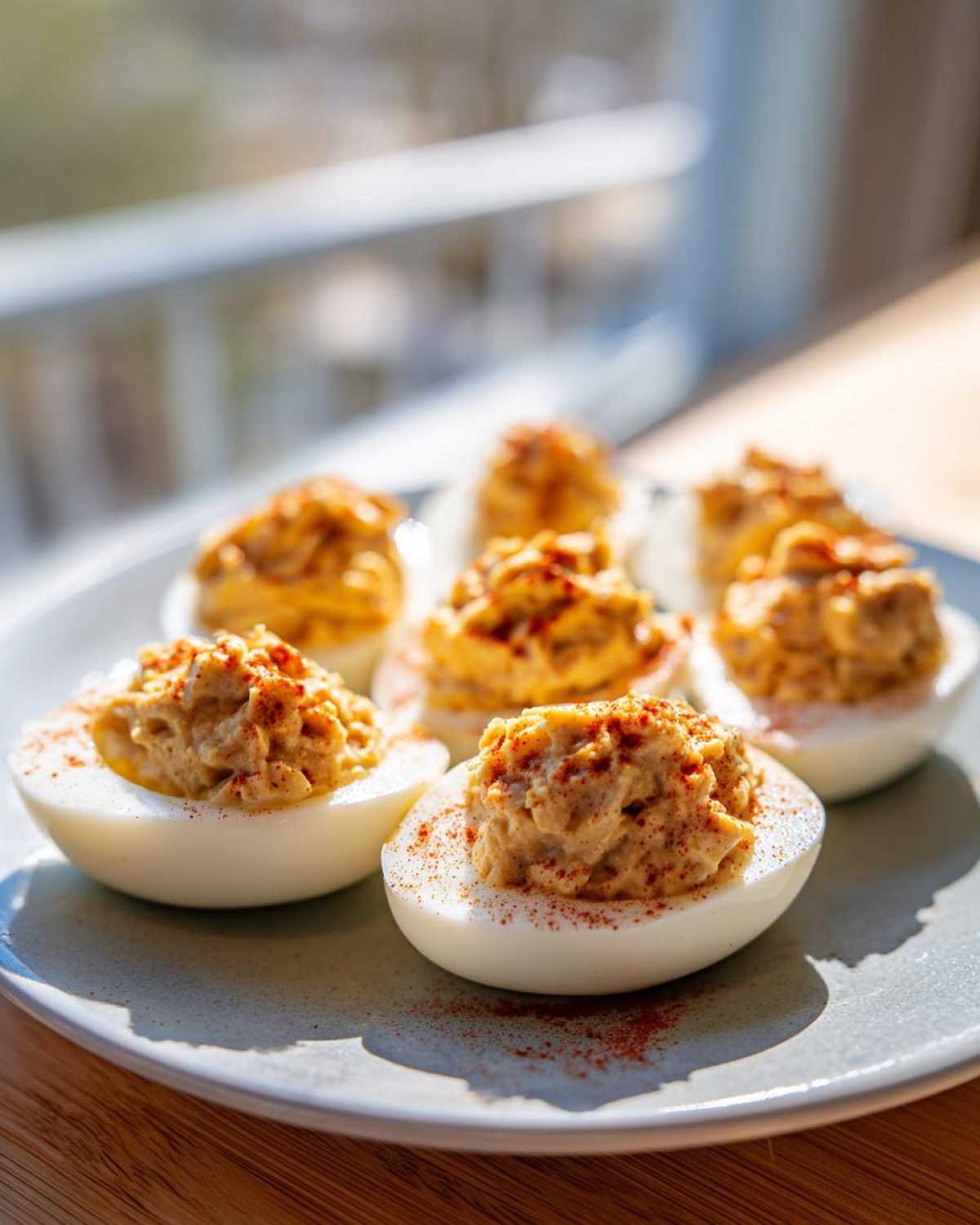 A close-up shot of several tuna deviled eggs on a light blue plate, garnished with paprika, in natural light.