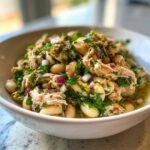 Close-up of a vibrant tuna white bean salad with parsley, red onion, and olive oil in a white bowl.