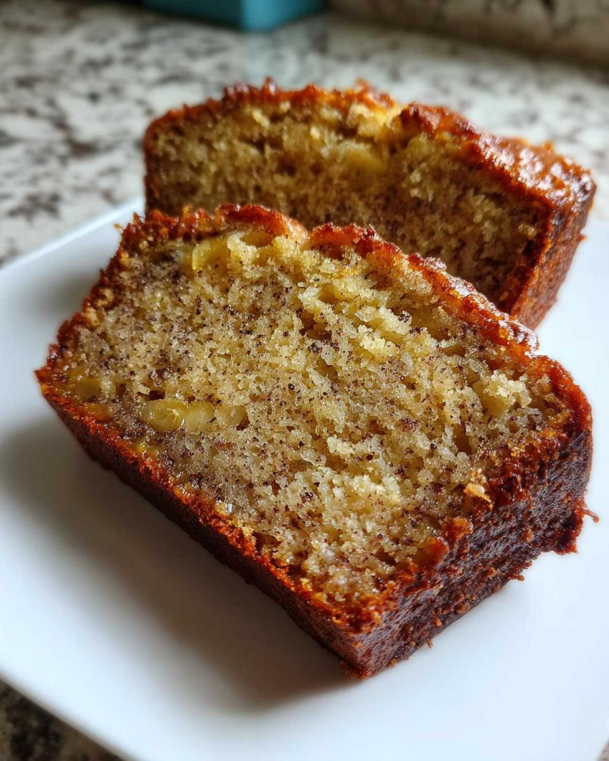 Two moist slices of golden brown protein banana bread on a white plate, showing the texture and specks of banana.
