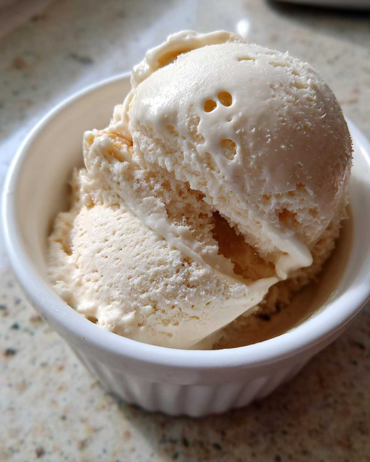 Close-up of a white bowl filled with scoops of creamy vanilla protein ice cream, showing its smooth texture.