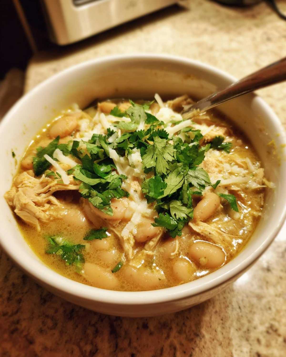 A bowl of creamy white chicken chili topped with shredded cheese and fresh cilantro.