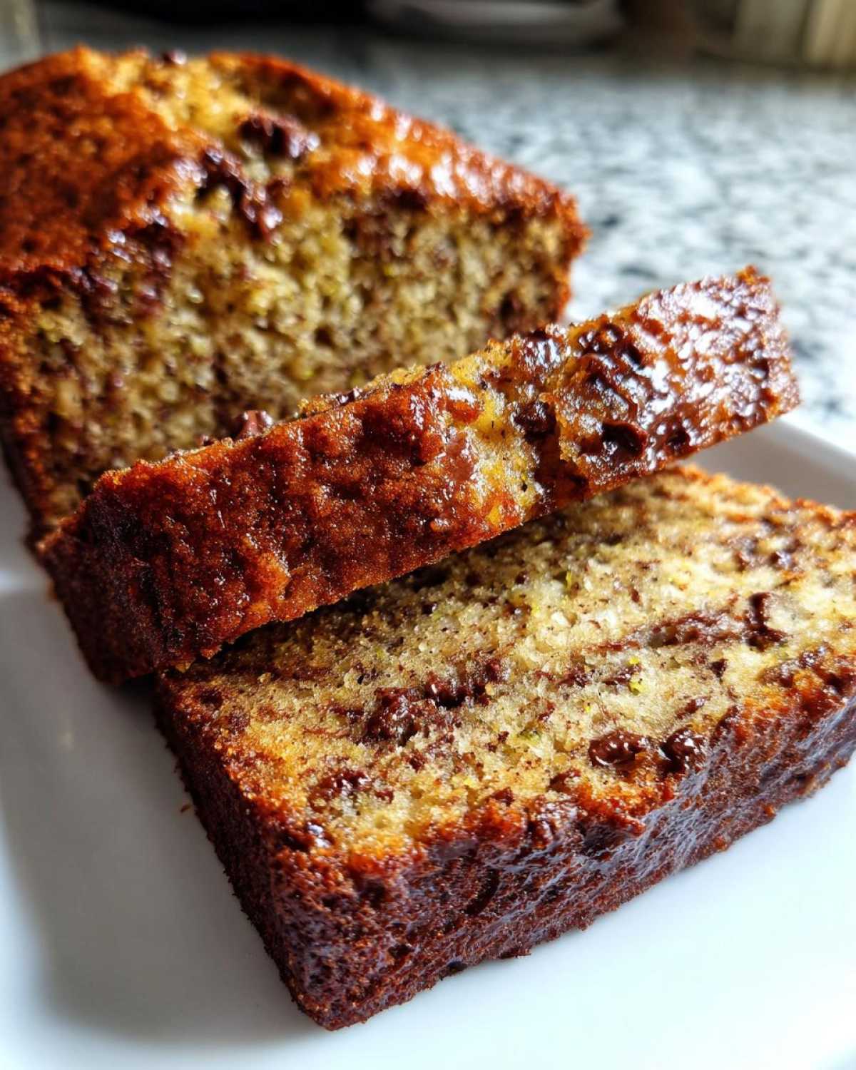 Two slices of moist zucchini bread with chocolate chips on a white plate, showcasing the texture and color.