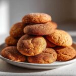 A stack of homemade apple cider cookies on a white plate, dusted with cinnamon sugar.