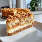 A delicious slice of apple crumble cheesecake with a graham cracker crust, creamy filling, apple layer, and crumble topping.