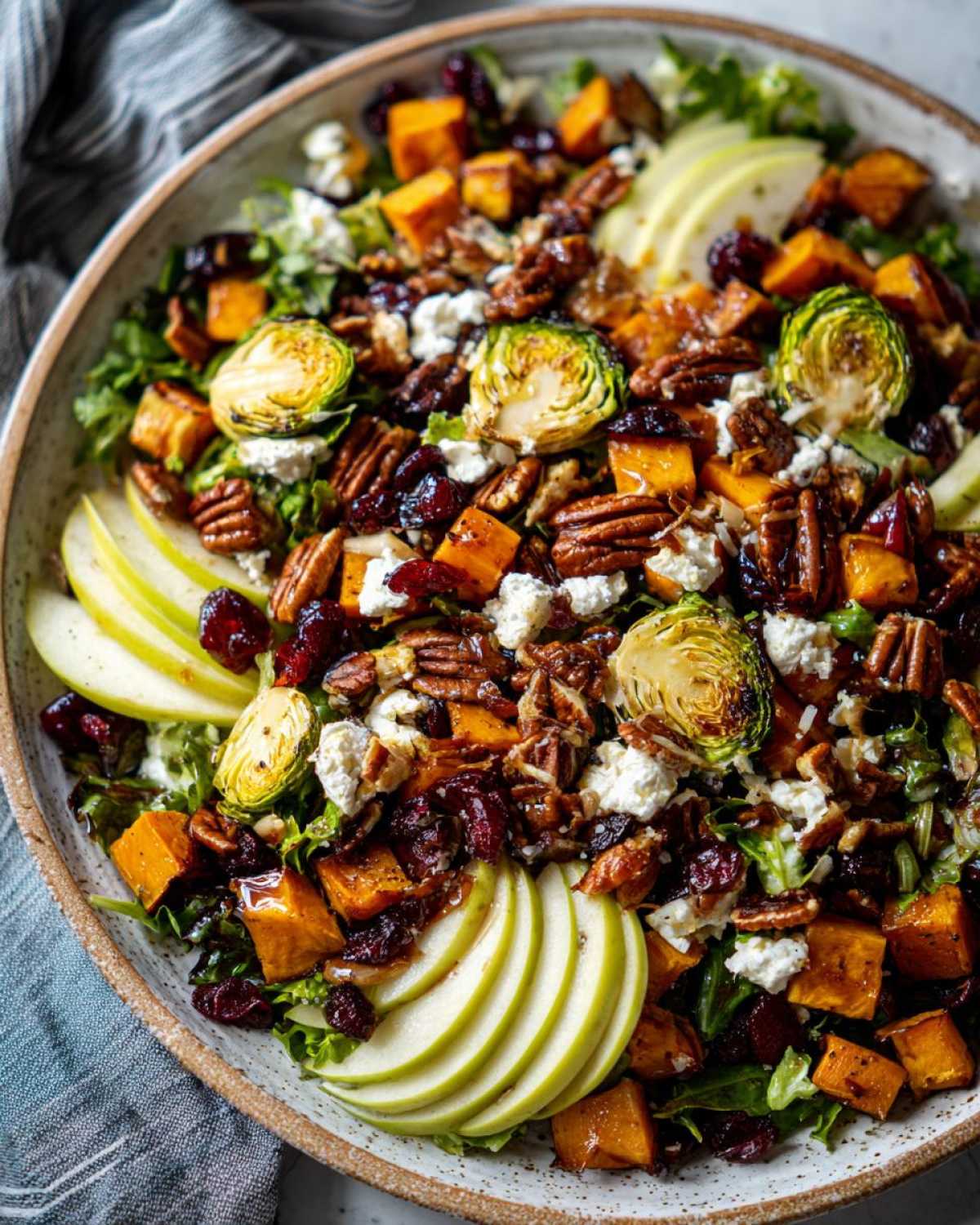 Overhead shot of a colorful autumn salad with apples, roasted butternut squash, pecans, cranberries, and goat cheese.