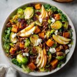 Overhead shot of a vibrant autumn salad with roasted butternut squash, pears, brussel sprouts, pecans, and goat cheese.