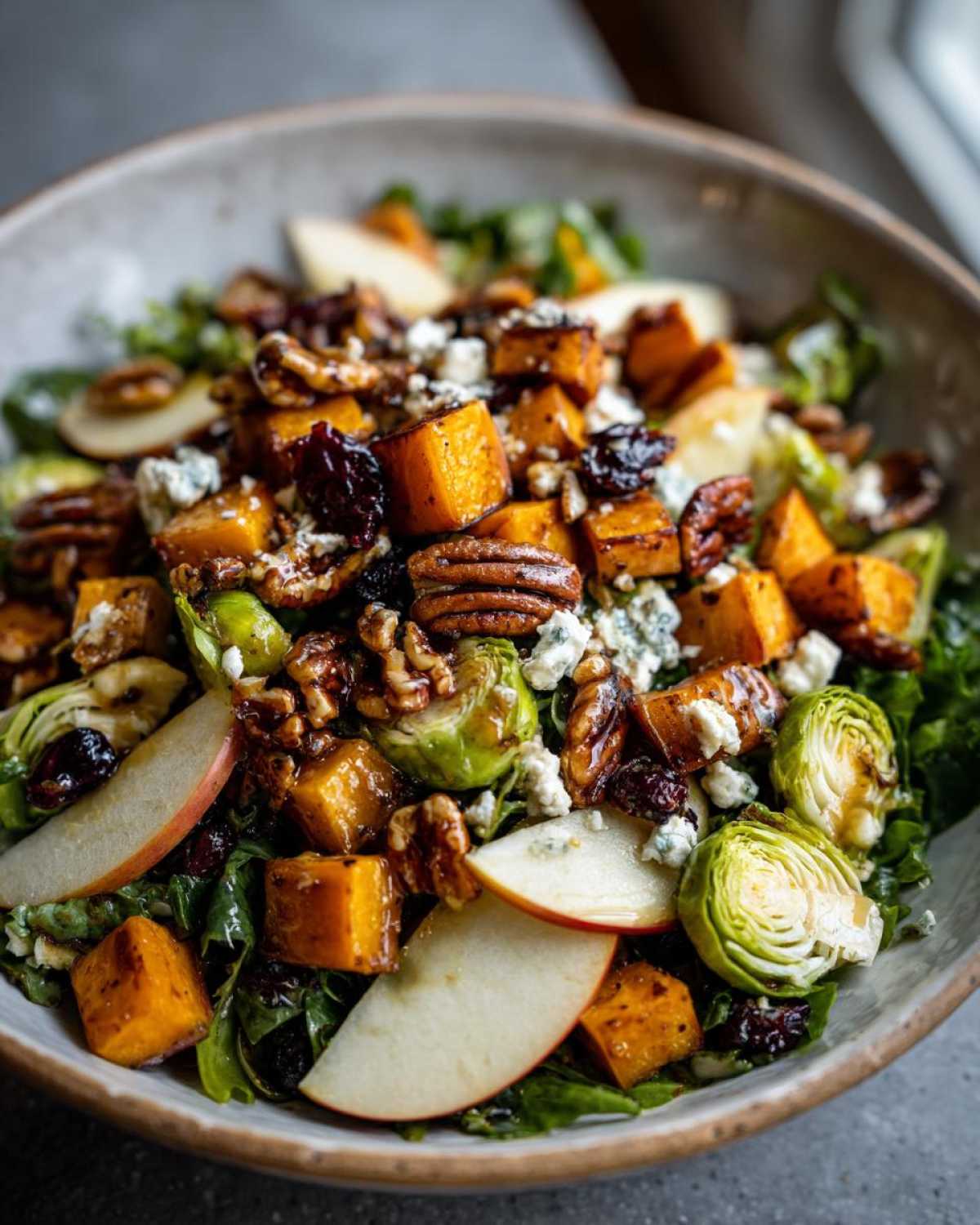 A vibrant autumn salad featuring roasted butternut squash, apples, Brussels sprouts, pecans, and blue cheese.