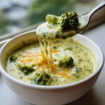 A spoonful of creamy broccoli cheddar soup with a cheesy pull, showcasing the texture and ingredients.