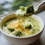 A spoonful of creamy broccoli cheddar soup with a cheesy pull, showcasing the texture and ingredients.
