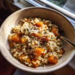 Close-up of a bowl of creamy butternut squash risotto topped with diced squash, grated parmesan, and fresh herbs.