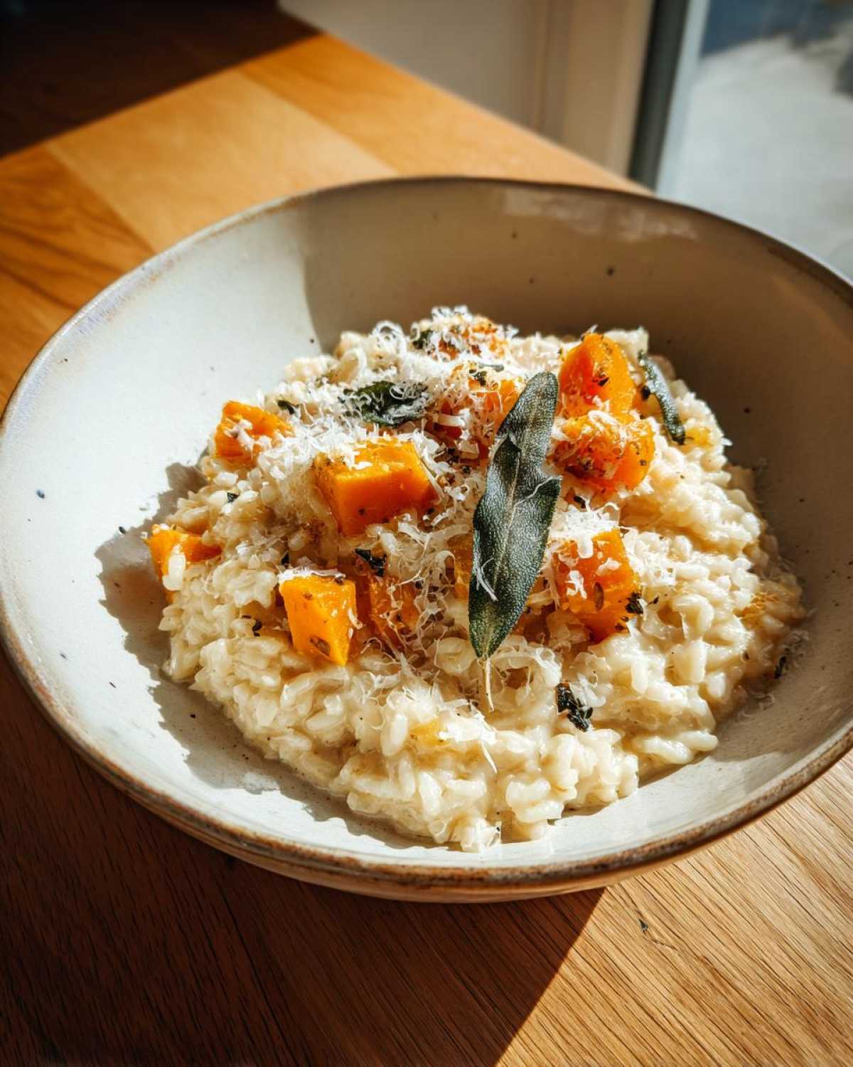 A close-up of creamy butternut squash risotto topped with roasted squash cubes, grated Parmesan cheese, and fresh sage leaves.