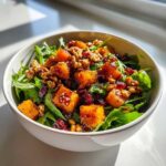 A close-up of a delicious butternut squash salad with fresh greens, roasted butternut squash cubes, walnuts, and dried cranberries.