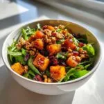 A close-up of a delicious butternut squash salad with fresh greens, roasted butternut squash cubes, walnuts, and dried cranberries.