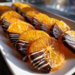 Close-up of glistening candied orange slices, half-dipped in dark chocolate and drizzled with white chocolate.