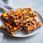 A plate piled high with chocolate bark topped with candy corn and pretzels, perfect for Halloween.