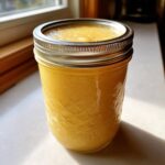 A sealed jar of canning applesauce sits on a windowsill, filled with golden homemade goodness.