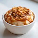 A close-up of creamy caramel apple dip topped with crunchy crumbs and drizzled with caramel sauce.