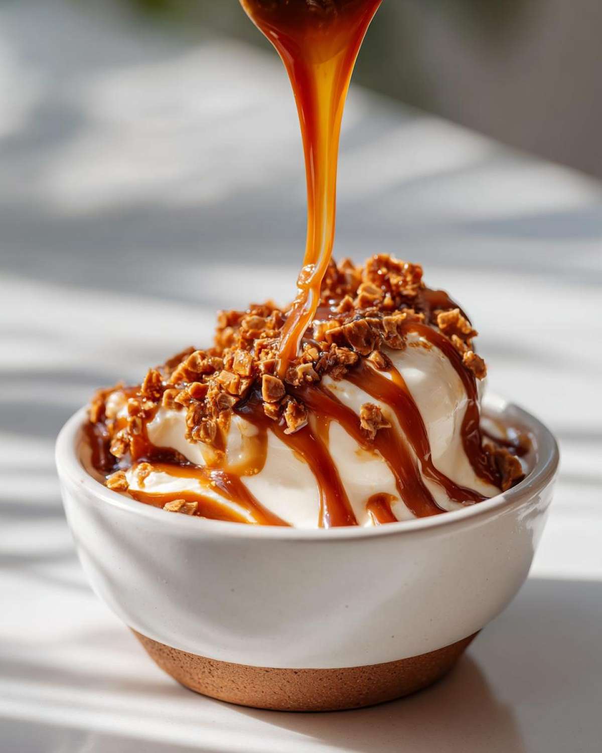 A close-up of creamy ice cream in a bowl being drizzled with rich caramel sauce and sprinkled with crunchy toffee bits, perfect for caramel apple dip.