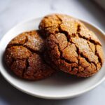 Close-up of three chewy molasses cookies with a cracked surface and sugar coating on a white plate.