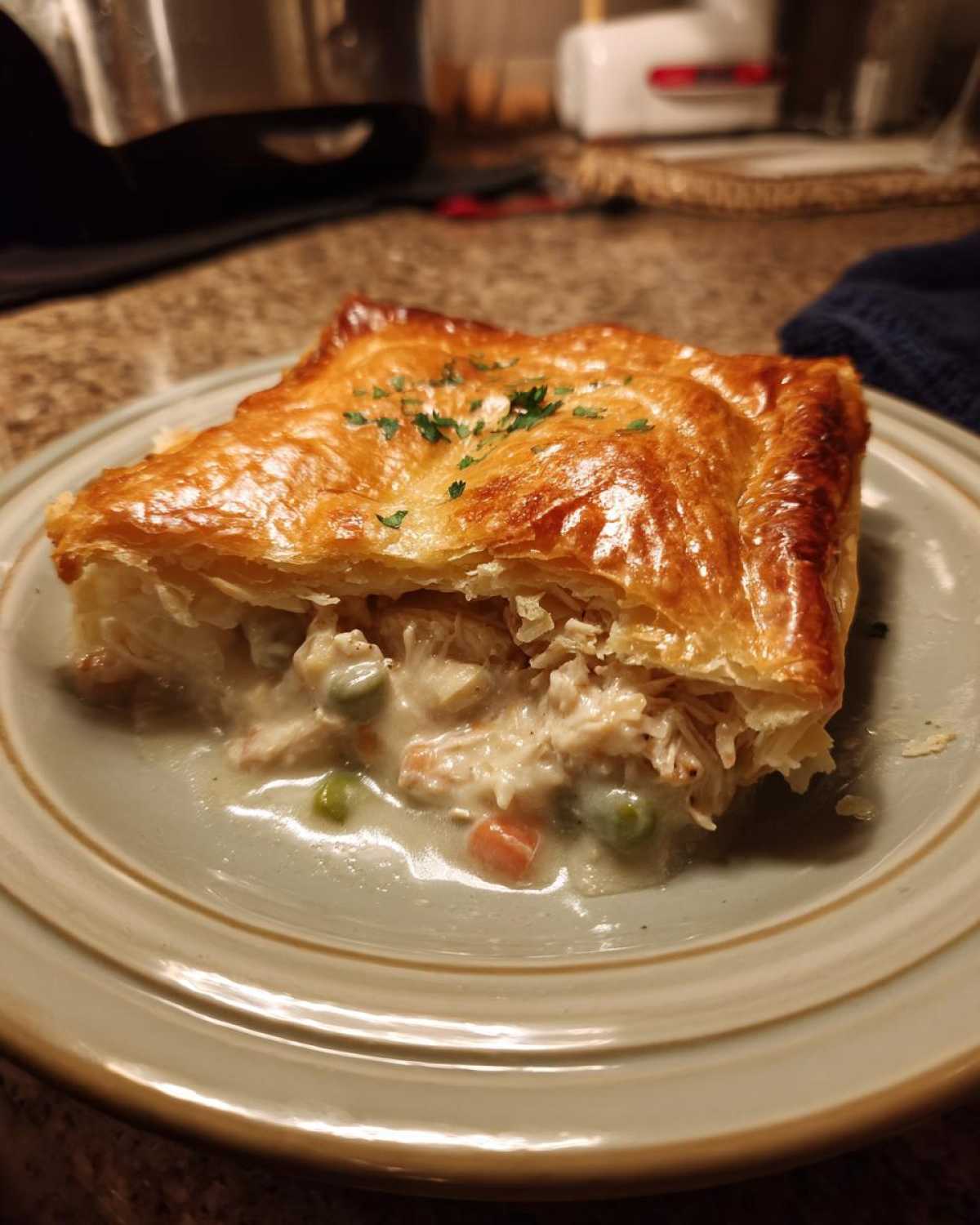A golden-brown slice of chicken pot pie with flaky crust, filled with creamy chicken and vegetables, garnished with parsley.