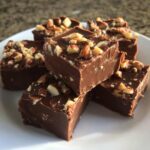 Delicious homemade chocolate fudge recipe topped with chopped almonds on a white plate.